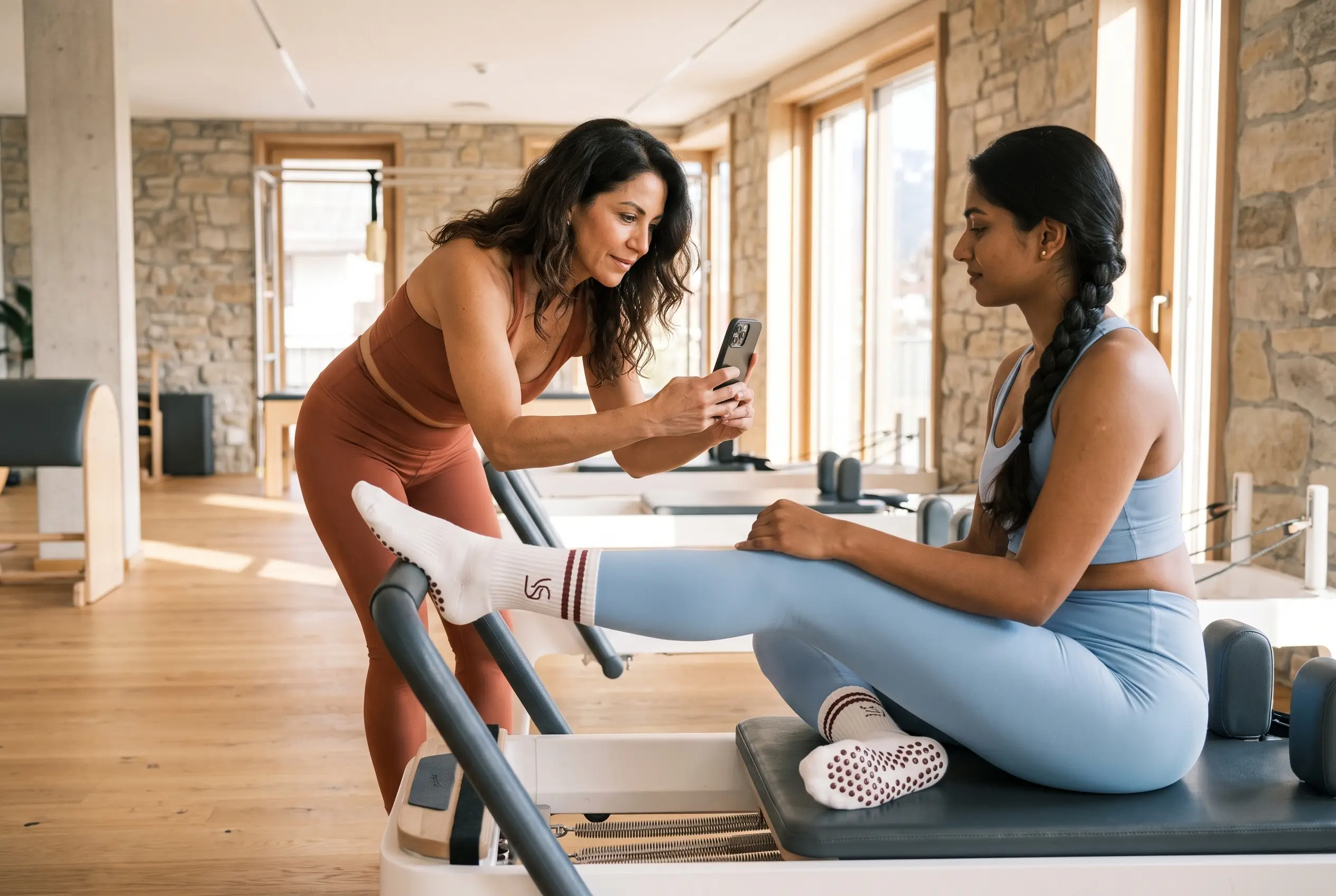 Boutique Pilates studio owner reviews local marketing plans on a laptop at reception, with branded grip socks and a bright class space behind.